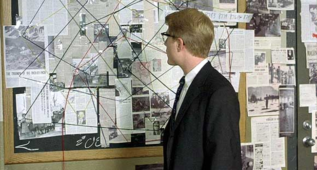 A detective looking at a wall which has pins with strings between them